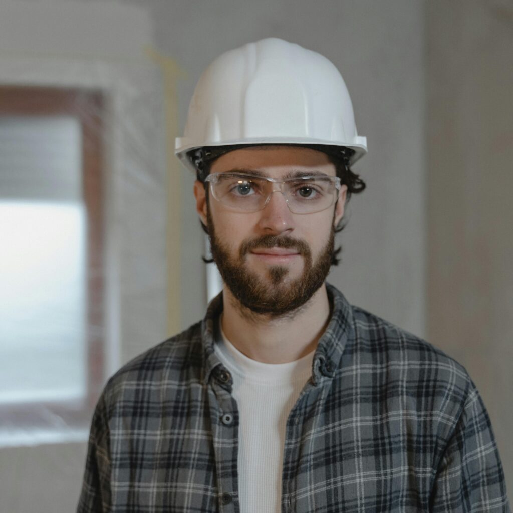 Portrait of a construction worker wearing a hard hat and safety glasses inside a building.